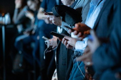 Hands of multiple graduates checking phones