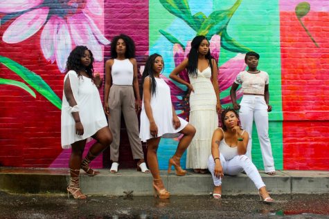 Six black teen women in white in front of colorful wall