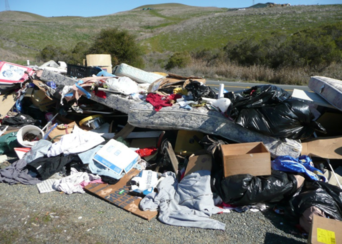 A pile of dumped mattresses, cardboard boxes and trash is seen on the side of a freeway. (Photo courtesy of Dylan Chiu, planner, Contra Costa County)
