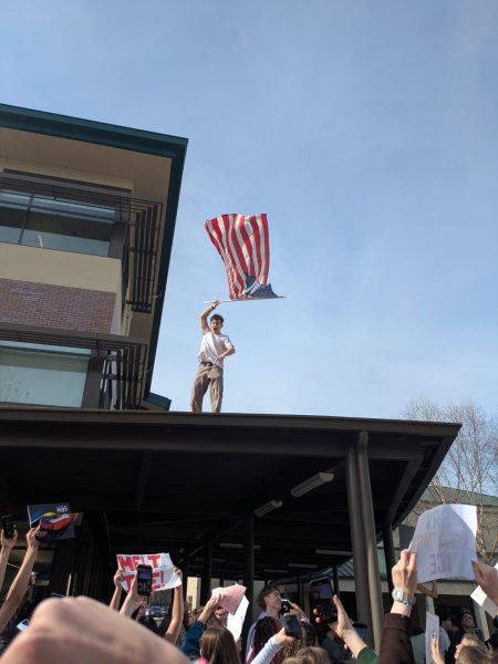 A San Ramon Valley High School student waves an American flag on a rooftop during a march on campus last week. (Photo by Kristina Minaeva via Contra Costa Youth Journalism)
